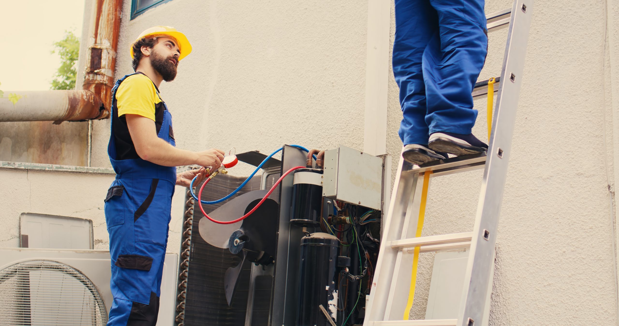 Proficient expert holding electric power drill stepping down from folding ladder after finishing servicing rooftop hvac system while coworker assembles manifold gauges to check freon levels